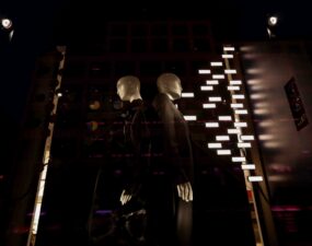 Ausgeleuchtete Schaufensterinszenierung mit Schaufensterpuppen und reflektierenden Lichtpunkten bei Nacht.