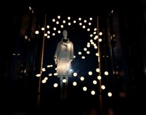 Ausgeleuchtete Schaufensterinszenierung mit Schaufensterpuppe und reflektierenden Lichtpunkten bei Nacht.