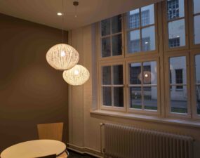 Kugelförmige Pendelleuchten aus Drahtgeflecht leuchten über einem kleinen Tisch vor einem Fenster.