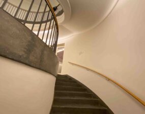 Treppenhaus im Museum Berggruen mit indirekter Deckenbeleuchtung, Betonstufen, weißem Wandverlauf und Holzhandlauf.