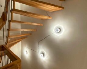 Runde Wandlampen noch ohne Verkleidung beleuchten die Wand entlang einer Holztreppe.