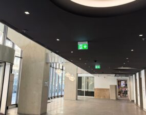 Lichtgestaltung im Atrium der Schellingstraße in Berlin mit einem modernen, abgedunkelten Deckenbereich, in dem eine runde Deckenbeleuchtung sanft strahlt. Im Hintergrund sind große Fenster zu sehen.