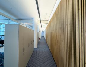 Langer Büroflur mit eingelassener Deckenbeleuchtung und Holzlamellenwand.