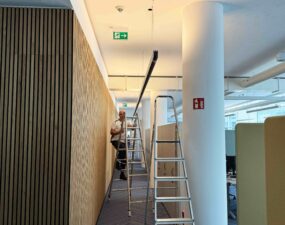 Elektriker montiert lineares Beleuchtungssystem an der Decke eines modernen Büroflurs.