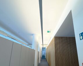Langer Büroflur mit eingelassener Deckenbeleuchtung und Holzlamellenwand.