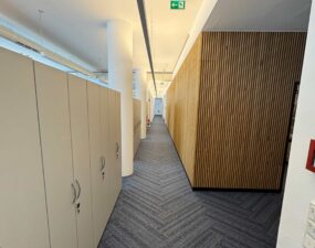 Langer Büroflur mit eingelassener Deckenbeleuchtung und Holzlamellenwand.