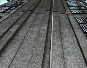 Perspektivische Untersicht einer strukturierten Betonfassade mit senkrechten Rillen und einer hellen LED-Lichtleiste in der Mitte.
