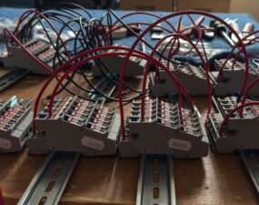 Werkbank mit mehreren grauen Reihenklemmen auf Hutschienen, verkabelt mit roten und schwarzen Kabeln.