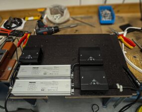 Werkbank mit zwei silbernen LED-Treibern der Marke PROLED sowie zwei schwarzen Anschlussgehäusen, umgeben von Werkzeug.