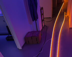 Flur mit einer geschwungenen, orange leuchtenden LED-Lichtlinie auf dem Boden, im Vordergrund violettes Umgebungslicht.
