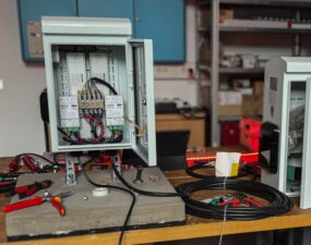 Offener grauer Schaltschrank mit zwei LED-Netzteilen und Klemmenblock, daneben aufgerollte Kabel auf einer Werkbank.