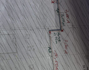Ausschnitt eines Dachplans mit handschriftlich eingetragenen Streckenmaßen in Rot und Grün an einer Gebäudeecke.